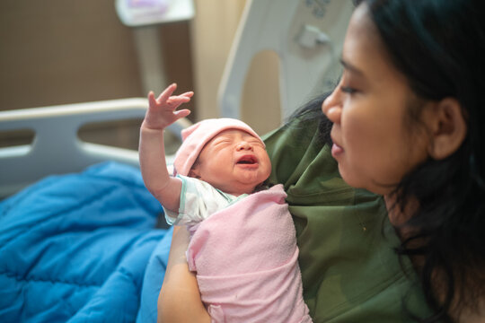 Mother holding crying newborn baby in hospital bed after childbirth