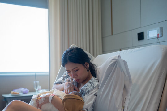 Asian mother breastfeeding her newborn baby girl in hospital bed after delivery