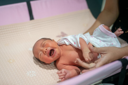 Crying newborn baby lying on a changing table while mother gently holds and dresses them.