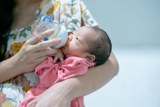 Close-up of a newborn baby being bottle-fed by a mother while cradled gently in her arms.