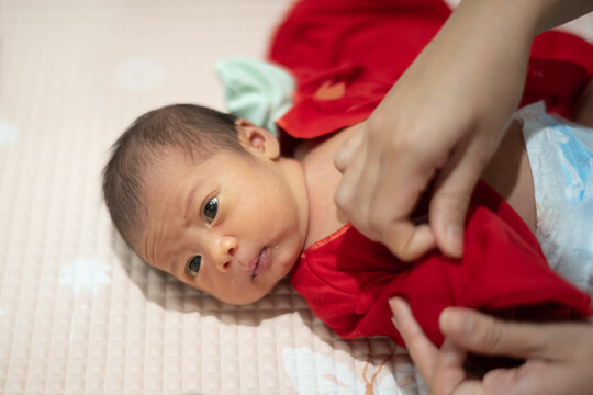 Mother hands gently dressing her awake newborn baby in a red outfit on a changing mat.