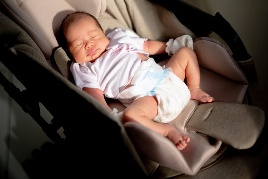 Peaceful newborn baby sleeping in a stroller bassinet with warm dramatic sunlight shining across.