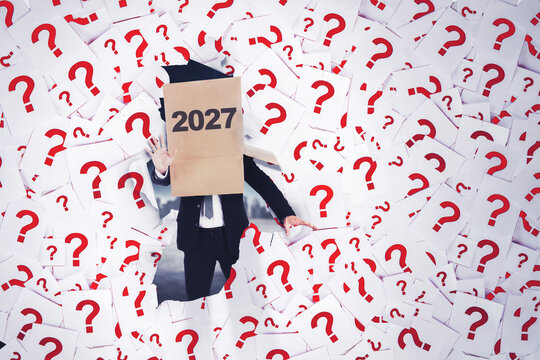 Businessman with 2027 Box on Head Breaking Through Question Marks
