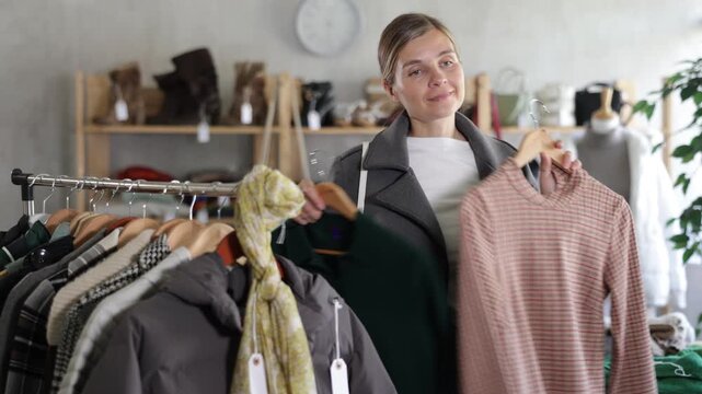 While shopping, woman browsing goods items and choose elect warm dress in store, buyer consider some items. Concept of seasonal wardrobe shopping. Client and holiday shopping