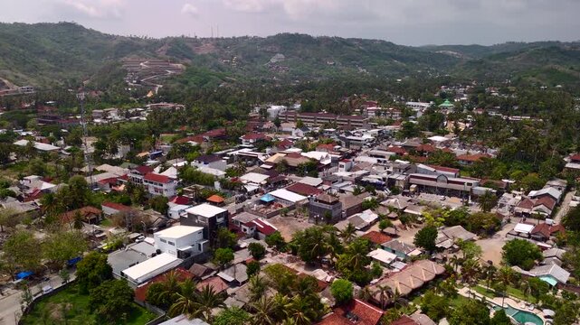 Drone view floats over tropical town rooftops roads palm trees and green hillside for travel documentary residential landscape and local island community content