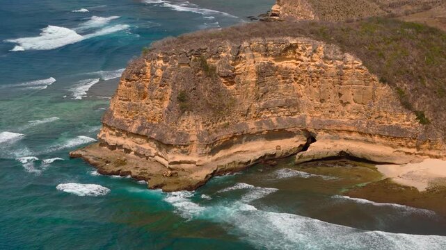 Drone view ekas reveals a sea cave carved into golden coastal cliff above shallow turquoise water for tropical geology adventure travel and natural landmark concepts