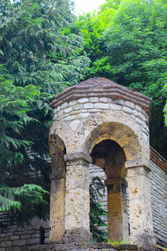 A small light-colored stone bell tower with a tiled roof. Greenery in the background. Bodbe, Kakheti, Georgia