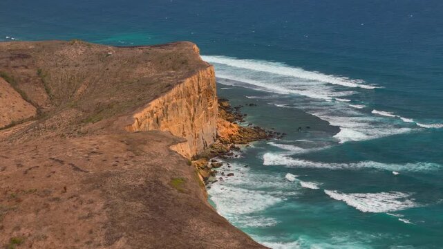 Aerial ekas view shows tall coastal plateau cliffs above narrow beach and long white surf lines for scenic travel nature geography and rugged shoreline projects
