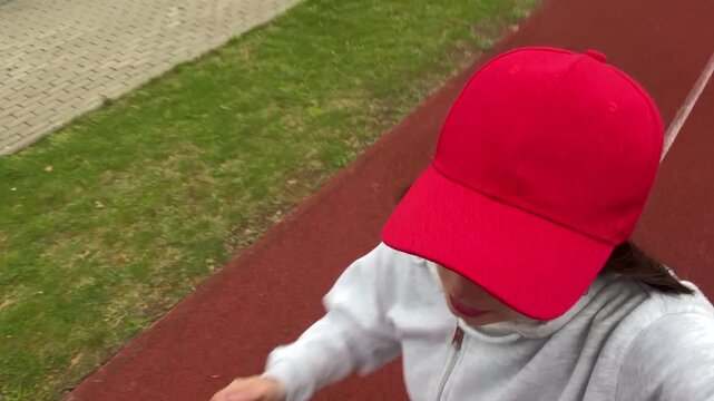 High angle POV selfie of a young active woman in a red cap running on an athletic track, horizontal smartphone video screenshot for fitness blogging and content creation concept