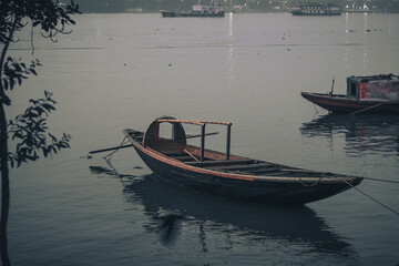 Obraz premium Traditional South Asian nouka wooden boat floating on the quiet waters of a river at twilight or overcast evening.
