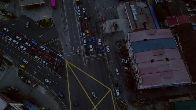vertical bird's eye view, cars and motorbikes driving through a yellow marked box junction in Port Klang, Malaysia. Smooth aerial view tilt up drone