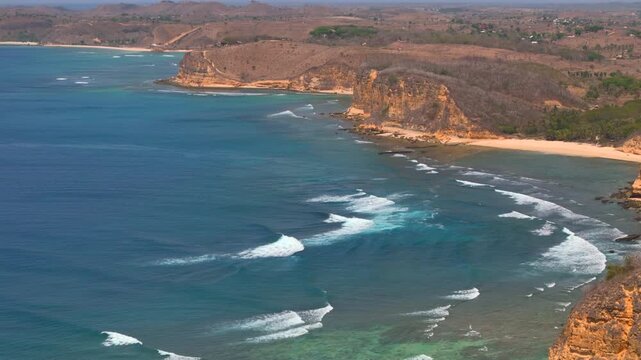 High drone ekas shot follows rugged cliff coastline with turquoise bays rocky shore and foaming ocean waves for tropical travel nature and coastal landscape imagery
