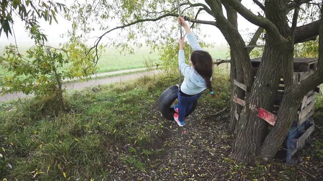 Slow Motion Teen girl swinging on a homemade bungee from rubber from car wheel near a large tree.