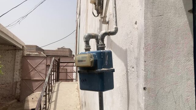 Blue utility gas meter with pipes installed on an exterior concrete residential wall