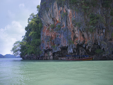 Traditional Thai rua hang yao Longtail Boat Moored Under Towering Mogote Limestone Cliff in Phang Nga Bay Thailand