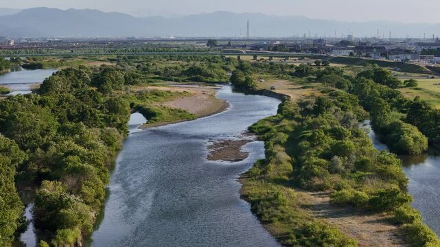 River meanders through lush greenery. Distant mountains rise behind the trees. Urban landscape fades into hazy horizon. No people, no animals, no movement. Ideal for nature, travel