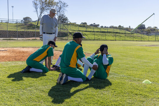 Baseball players kneeling and assessing after seated player holding head, coach watching near cone
