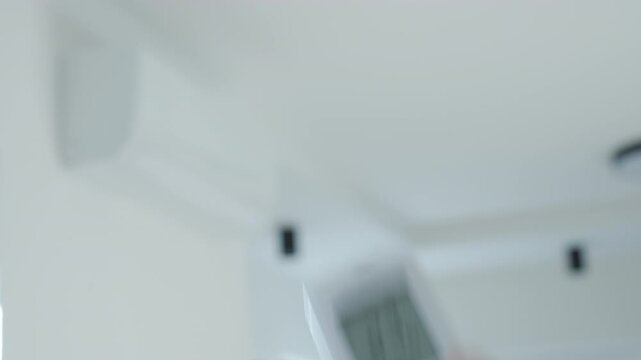 Hand sets air conditioner temperature with a remote control indoors. Concept of home cooling, air conditioning and summer comfort