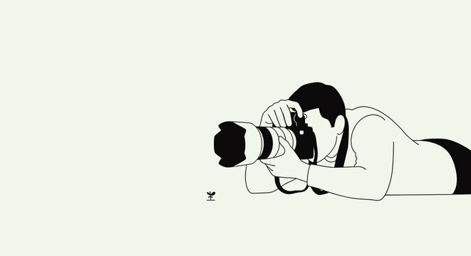 A photographer lying down on the ground capturing a tiny subject with a professional camera.