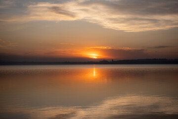 Obraz premium Serene sunset over a calm lake with reflections and distant silhouette of buildings
