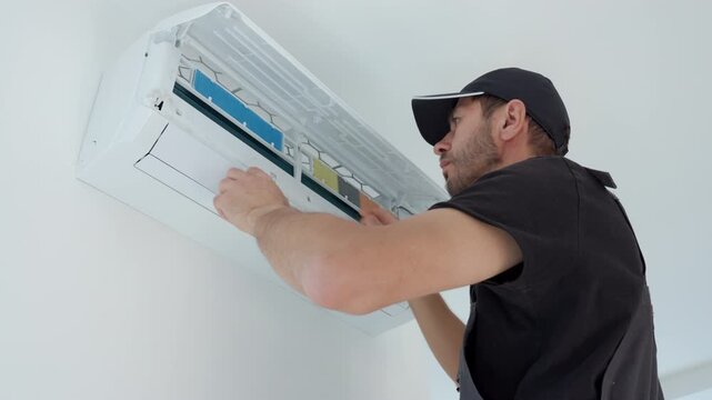 Man opens air conditioner to inspect or clean filters indoors. Technician lifts white cover of wall mounted split AC unit. Concept of AC maintenance, HVAC service and home appliance care
