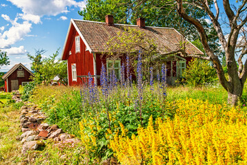 Red country house with vibrant flowering plants in a summer garden © Lars Johansson