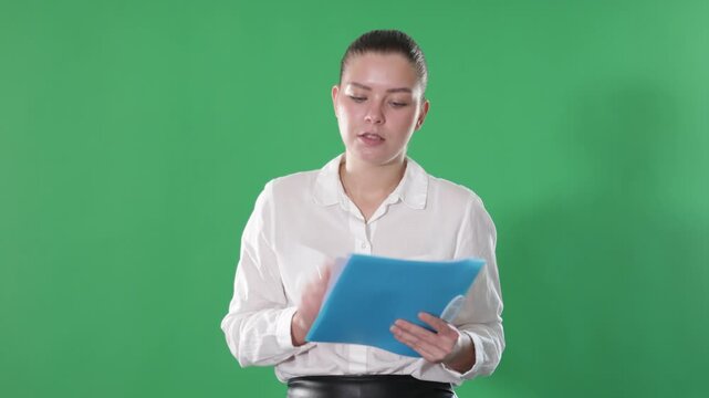 Young woman in a white blouse and a black skirt holds documents with a pen against the background of chrome key. Office employee fills out papers on a green background. High quality 4k footage