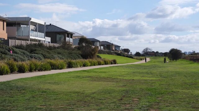 A premium, contemporary two-story houses overlooking a wide, green coastal linear park and shared pedestrian pathway in Werribee South, Melbourne, Australia