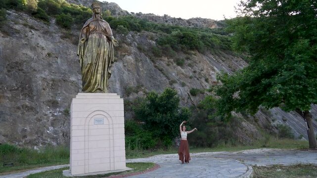 Cinematic wide shot of a dancing woman near the historic statue of Virgin Mary