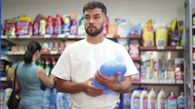 Man view trademark sign on label, chooses eco friendly liquid detergent of specific manufacturer. Customer examines product, reads composition on label