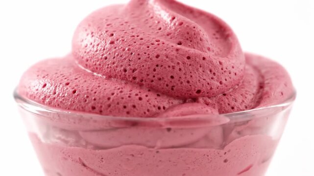 Extreme close-up of fluffy pink dessert mousse or whipped fruit sorbet in a glass dish, isolated on white, showcasing the light, aerated texture.