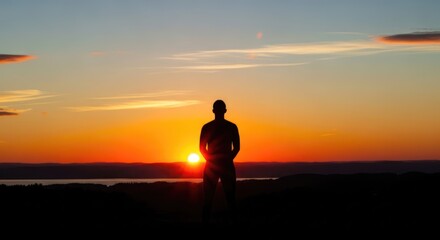 Obraz premium A silhouette of a person standing against a vibrant sunset sky, overlooking a distant landscape with a body of water in the horizon. 