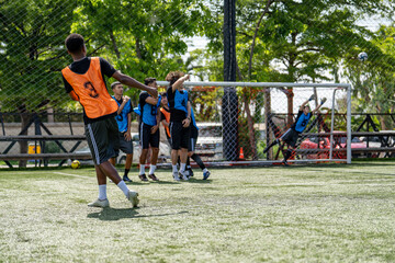 Fototapeta premium African American soccer player taking free kick shot during football match. Diverse opponents defensive wall standing near goal post waiting for ball outdoor