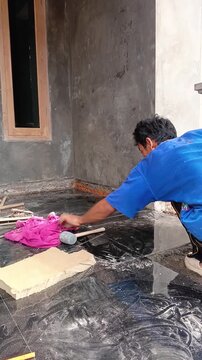 Construction worker applying cement grout between black granite floor tiles on terrace