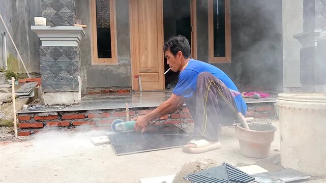 Construction worker cutting ceramic tile with angle grinder machine outdoors