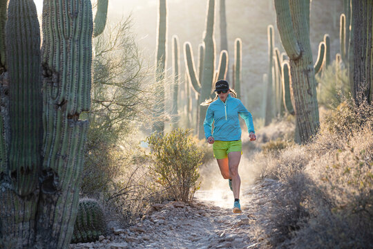 Woman runs along a desert trail lined with cactus in Tucson, Arizona.