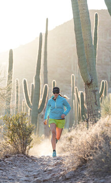 Woman runs along a desert trail lined with cactus in Tucson, Arizona.