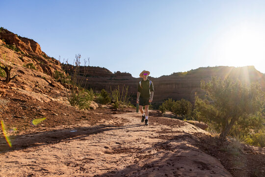 Young man hiking on a sunny desert canyon trail at sunrise