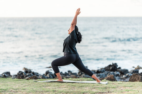 Woman practicing yoga warrior pose on a mat overlooking the ocean