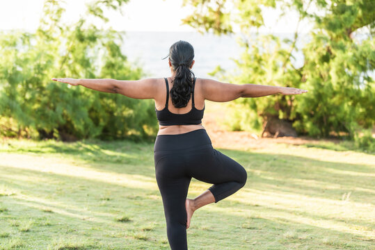 Back view of woman practicing yoga tree pose outdoors near the beach