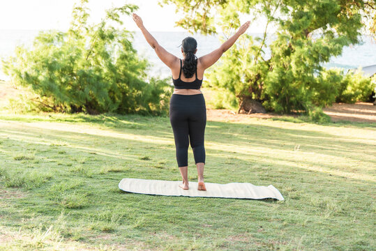 Back view of woman practicing yoga tree pose outdoors near the beach