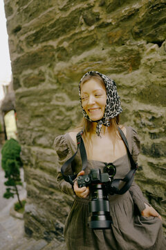 Female wedding photographer smiling with camera by stone castle wall