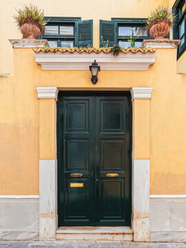 Historic yellow facade with a dark green entrance door and potted plants in the charming Plaka district, Athens.