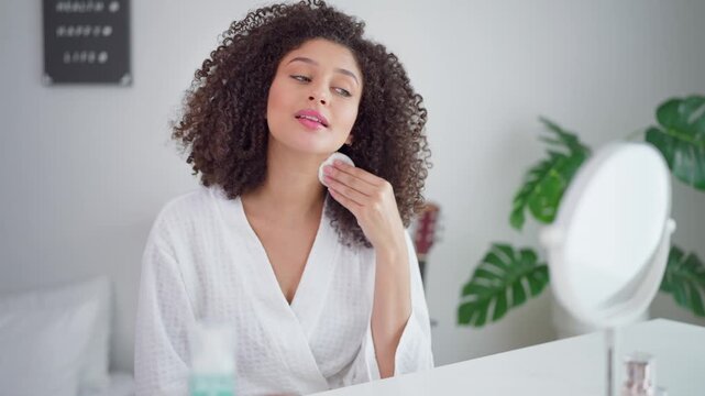 Latino young woman cleaning face with cotton pad and cleansing product. 