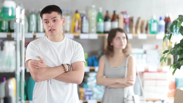 Young woman stands in a supermarket upset and resentful of a man who is standing in the background and talking emotionally. Couple quarrels in the hardware store