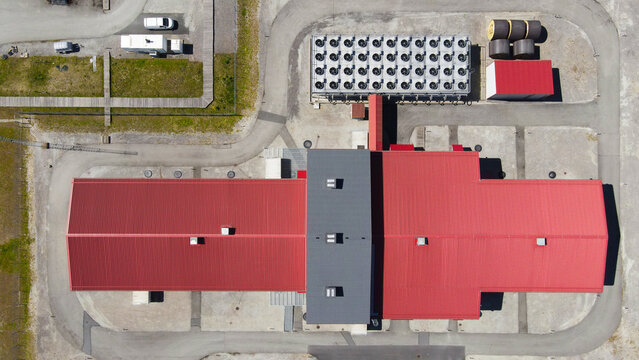 Aerial view showing a large industrial facility or data center with red roofs and a significant cooling system consisting of numerous fans, indicating high power consumption and infrastructure