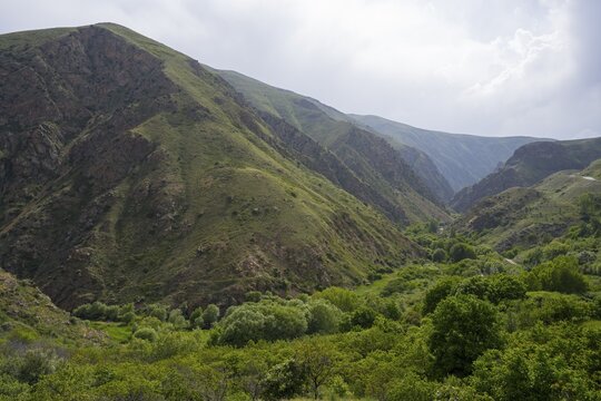 Green valley nestled between towering mountains under a partly cloudy sky, view from Vorotnavank Monastery, Vorotnavank, situated in the Vorotan Valley, Syunik Province, Armenia