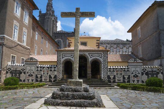 Ein altes Steinkreuz steht im Hof vor einem Mosaikdekorierten Geb&auml;ude unter blauem Himmel, ehemaliges Klosters, Convento de Santa Cruz, Mata Nacional do Bu&ccedil;aco, National-Wald von Bussaco, Bucaco, Mealhada, Beira Litoral, Portugal