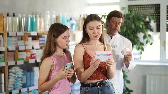 Woman with teen girl are busy choosing tablet pills at pharmacy. Man pharmacist in background. High quality 4k footage