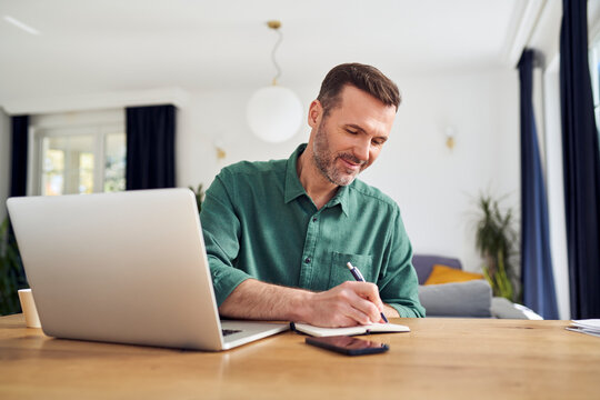 Handsome man working from home taking notes at desk